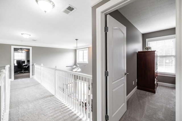 corridor featuring baseboards, carpet, a textured ceiling, and visible vents