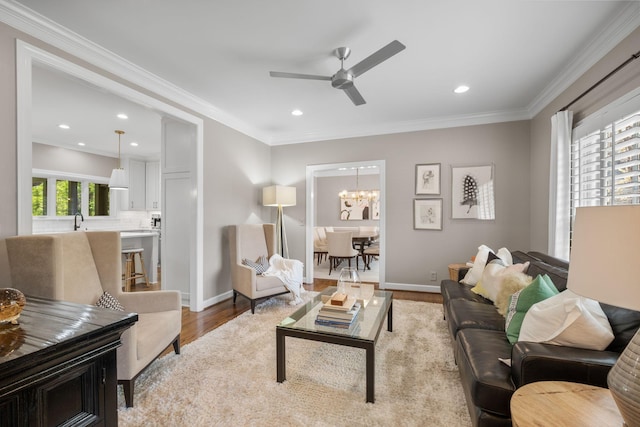living area featuring wood finished floors, recessed lighting, ornamental molding, and ceiling fan with notable chandelier