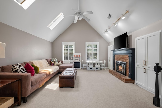 living room featuring a fireplace, ceiling fan, lofted ceiling with skylight, visible vents, and light colored carpet