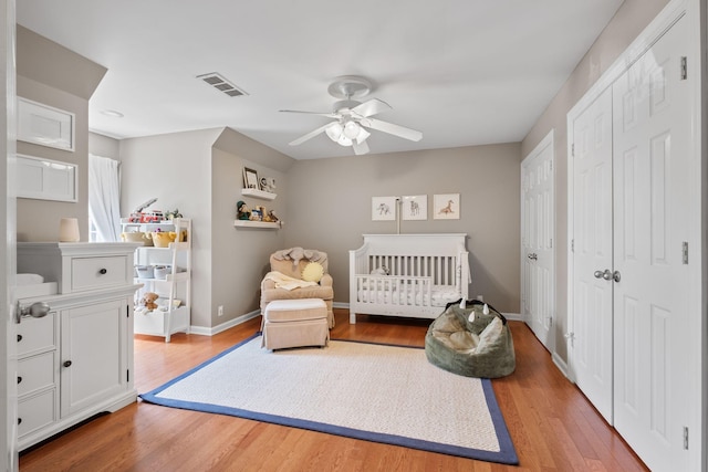 bedroom featuring ceiling fan, visible vents, a nursery area, baseboards, and wood finished floors