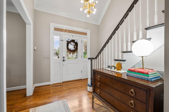 foyer with baseboards, ornamental molding, wood finished floors, a notable chandelier, and stairs