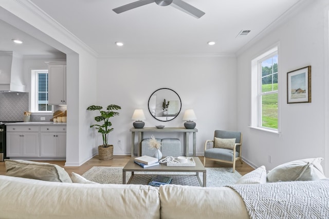 living area featuring visible vents, ornamental molding, a ceiling fan, and light wood finished floors