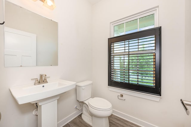 half bathroom with baseboards, toilet, and wood finished floors
