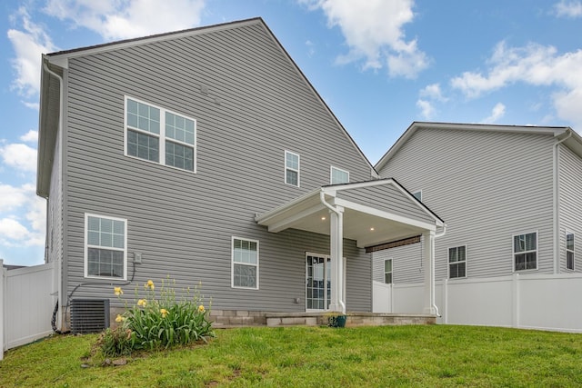 rear view of property featuring a lawn, central AC, and fence