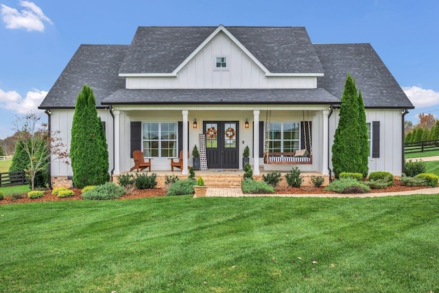modern farmhouse featuring covered porch, fence, board and batten siding, and a front lawn