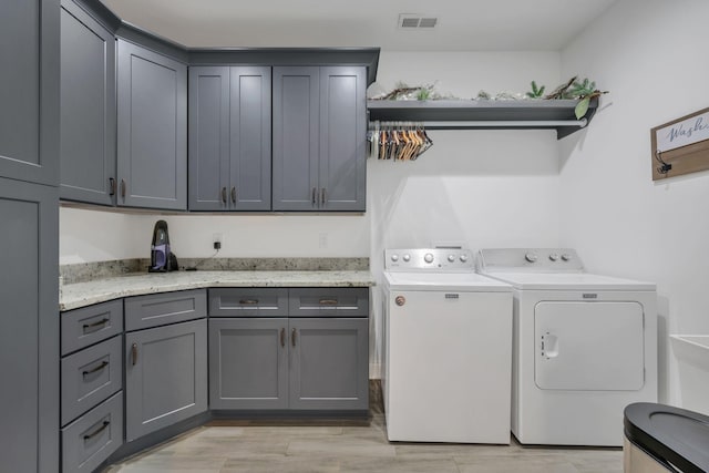 washroom with light wood-type flooring, washing machine and dryer, cabinet space, and visible vents