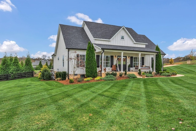 back of house featuring a porch, a shingled roof, a yard, board and batten siding, and fence