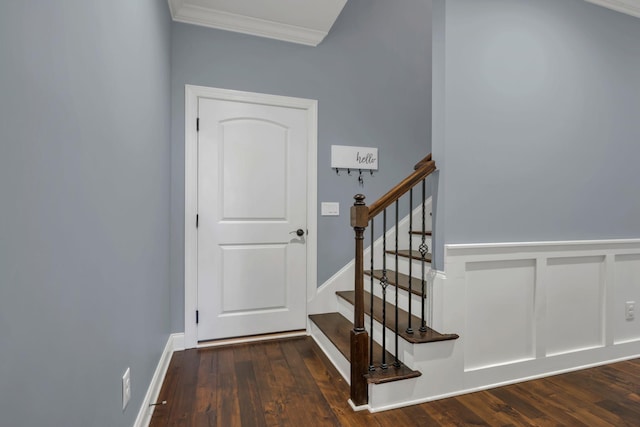 staircase with a wainscoted wall, wood finished floors, crown molding, and a decorative wall