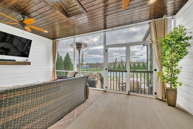 sunroom / solarium featuring a ceiling fan, wooden walls, and expansive windows