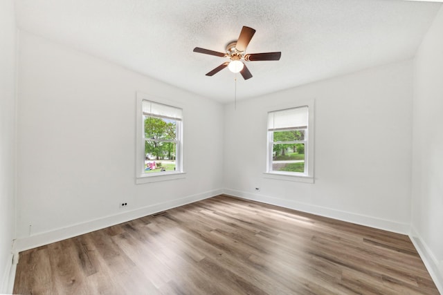 spare room featuring wood finished floors, a healthy amount of sunlight, a ceiling fan, and visible vents