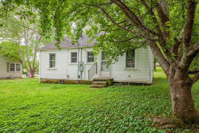back of house with a lawn, entry steps, and roof with shingles