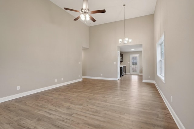 interior space featuring high vaulted ceiling, baseboards, wood finished floors, and ceiling fan with notable chandelier
