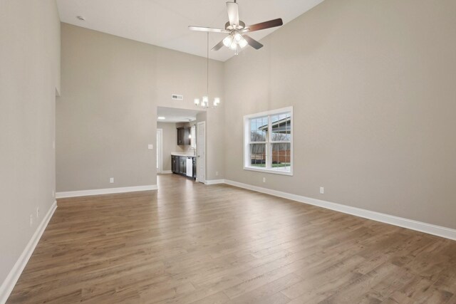 unfurnished living room featuring wood finished floors, baseboards, high vaulted ceiling, and ceiling fan with notable chandelier