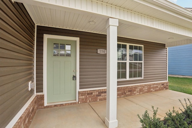 doorway to property with a porch and brick siding