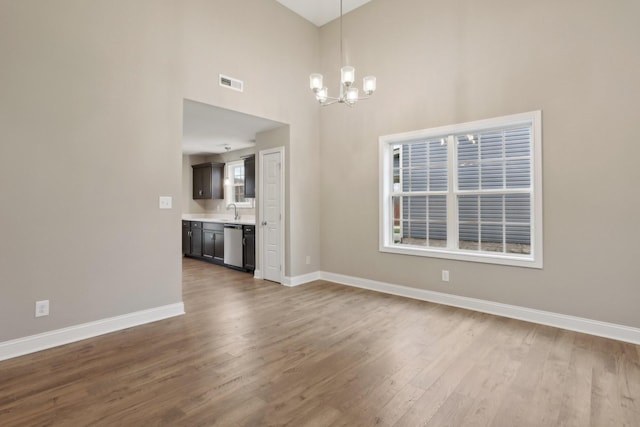 unfurnished dining area featuring an inviting chandelier, wood finished floors, visible vents, and baseboards