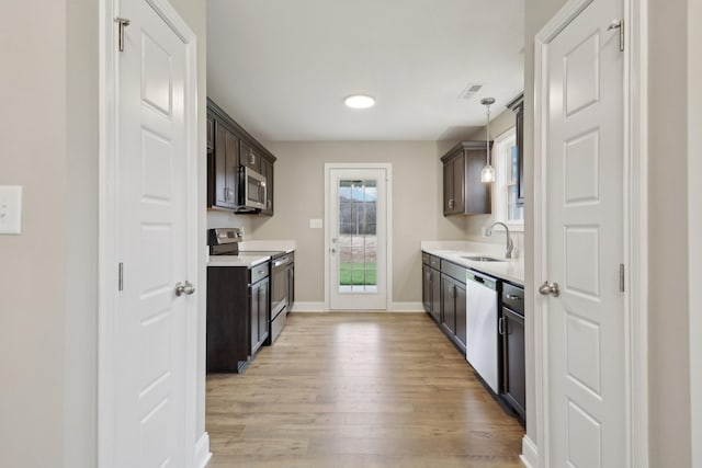 kitchen featuring appliances with stainless steel finishes, light wood-type flooring, light countertops, and a sink