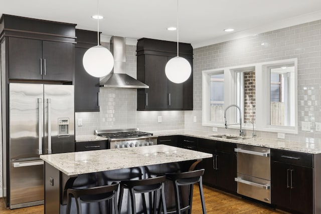 kitchen with a breakfast bar, stainless steel appliances, a kitchen island, wall chimney range hood, and a sink