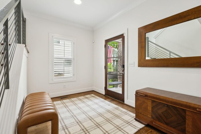 doorway to outside featuring baseboards, visible vents, wood finished floors, and ornamental molding