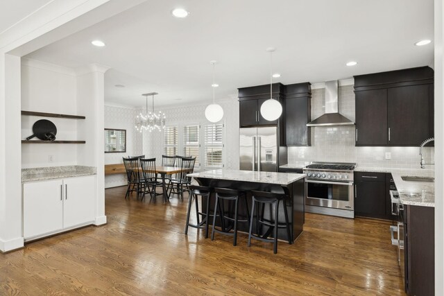 kitchen with wall chimney range hood, crown molding, a sink, a breakfast bar, and high quality appliances