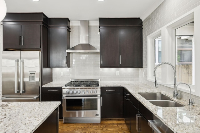 kitchen with tasteful backsplash, light stone counters, stainless steel appliances, wall chimney range hood, and a sink