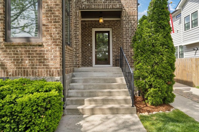 doorway to property featuring fence and brick siding