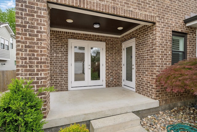 view of exterior entry with a patio, brick siding, french doors, and fence