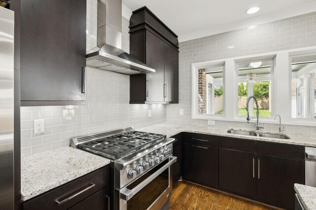 kitchen with stainless steel appliances, backsplash, a sink, dark wood-style floors, and wall chimney exhaust hood