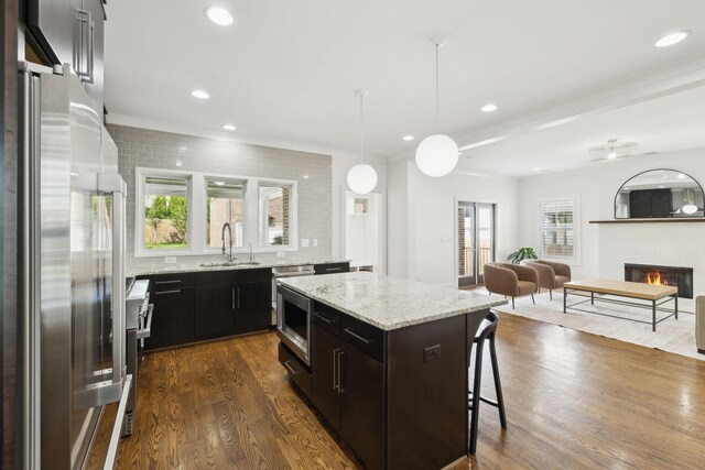 kitchen featuring a kitchen breakfast bar, a sink, a lit fireplace, dark wood-type flooring, and high quality appliances
