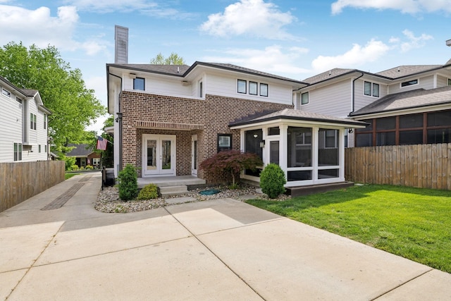 view of front facade featuring a chimney, brick siding, fence, and a sunroom