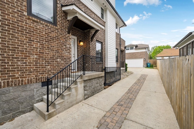 property entrance featuring a detached garage, brick siding, and fence