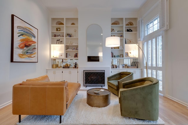 sitting room with light wood-type flooring, crown molding, built in features, and baseboards