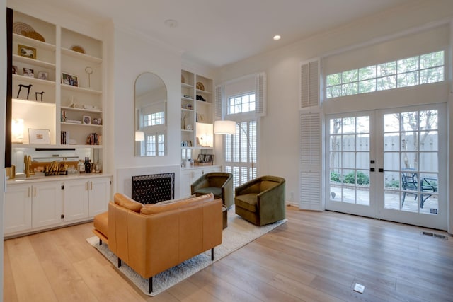 living room with crown molding, visible vents, light wood-type flooring, french doors, and built in features