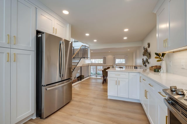 kitchen featuring light wood finished floors, recessed lighting, stainless steel appliances, a peninsula, and white cabinetry