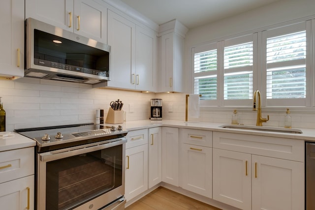 kitchen featuring stainless steel appliances, light countertops, backsplash, a sink, and white cabinetry