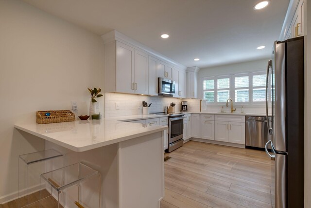 kitchen with tasteful backsplash, appliances with stainless steel finishes, white cabinets, a sink, and a peninsula