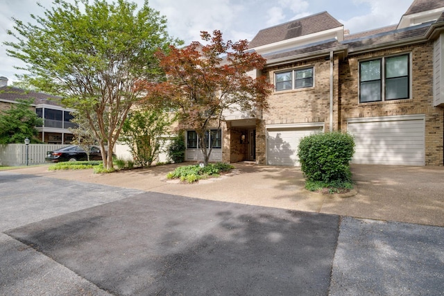 townhome / multi-family property featuring driveway, roof with shingles, brick siding, and an attached garage