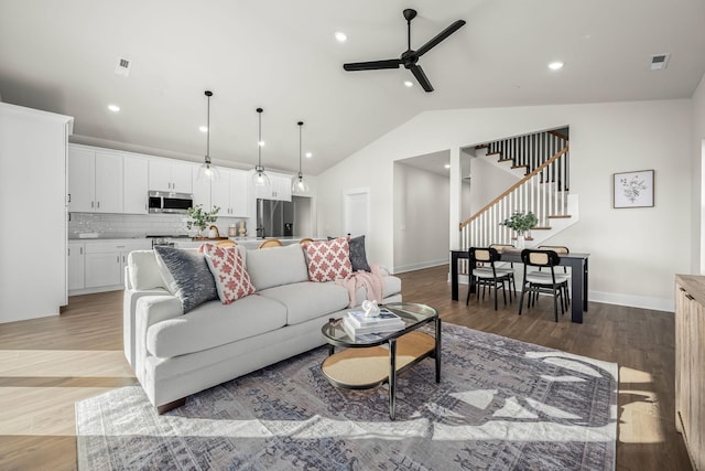 living room featuring lofted ceiling, stairway, light wood-type flooring, and a ceiling fan