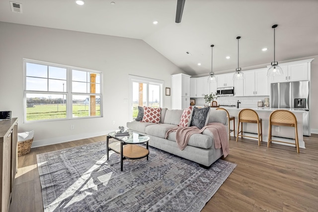 living room featuring lofted ceiling, visible vents, plenty of natural light, recessed lighting, and wood finished floors