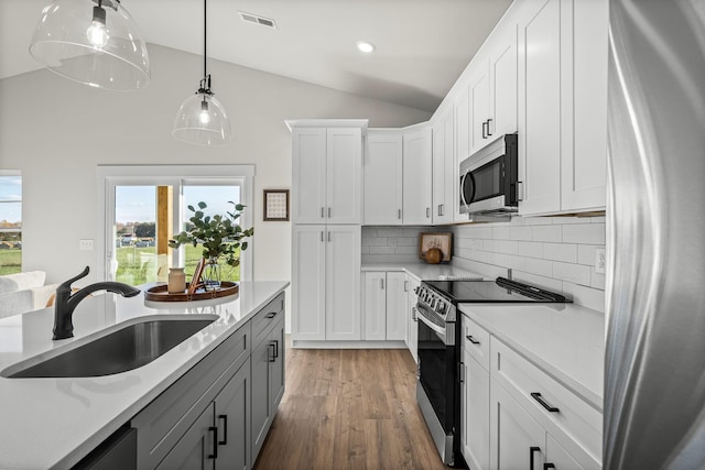 kitchen with a sink, gray cabinetry, stainless steel appliances, vaulted ceiling, and backsplash
