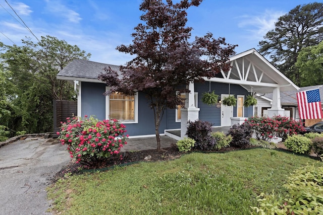 view of front of property featuring covered porch, a shingled roof, and a front lawn