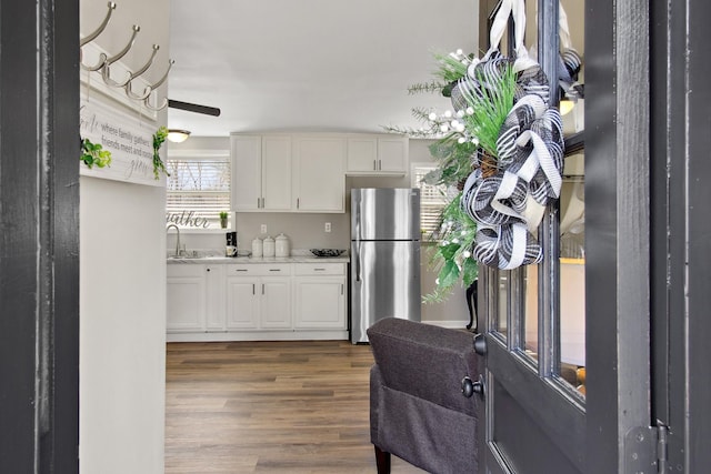 kitchen with wood finished floors, freestanding refrigerator, light countertops, white cabinets, and a sink
