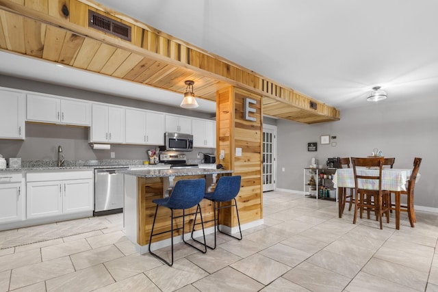 kitchen with light stone counters, a breakfast bar, appliances with stainless steel finishes, a sink, and visible vents