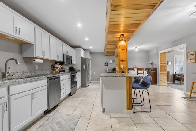 kitchen featuring recessed lighting, light stone counters, appliances with stainless steel finishes, a kitchen bar, and a sink