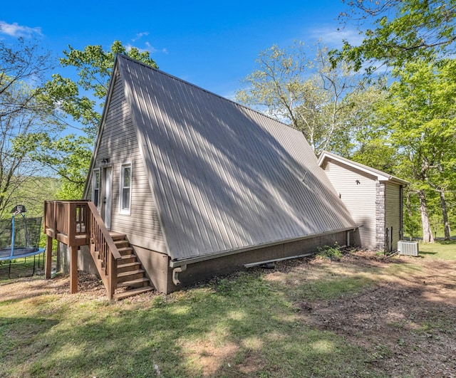 view of home's exterior with a lawn, cooling unit, metal roof, and a trampoline