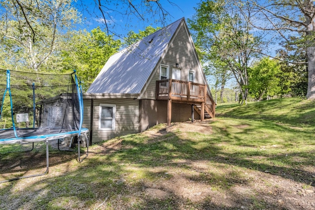 back of property with a wooden deck, a trampoline, metal roof, a lawn, and stairway
