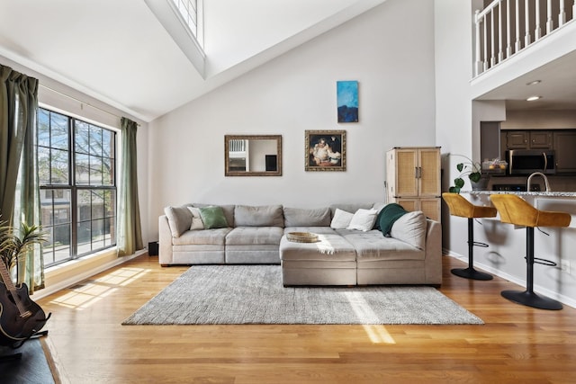 living room with baseboards, high vaulted ceiling, and light wood-style floors
