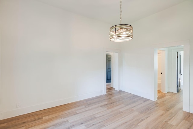 empty room with an inviting chandelier, baseboards, and light wood-type flooring