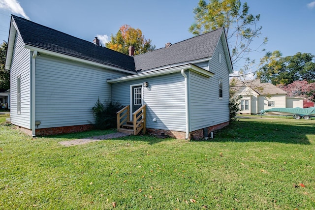 rear view of property with a lawn, a shingled roof, entry steps, and crawl space
