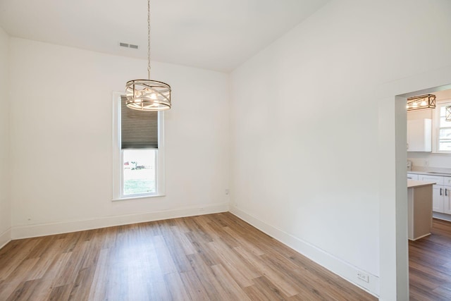 unfurnished dining area with visible vents, an inviting chandelier, baseboards, and light wood-style floors