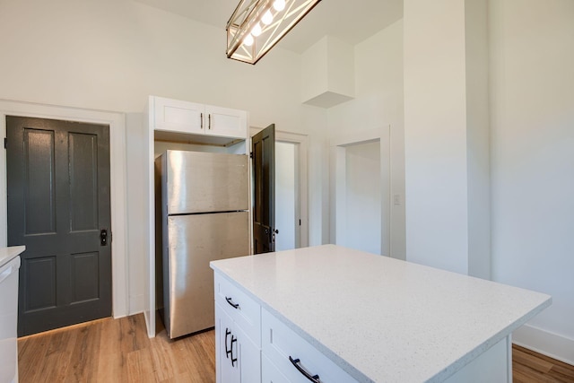kitchen with a high ceiling, light wood-style floors, white cabinetry, a kitchen island, and freestanding refrigerator